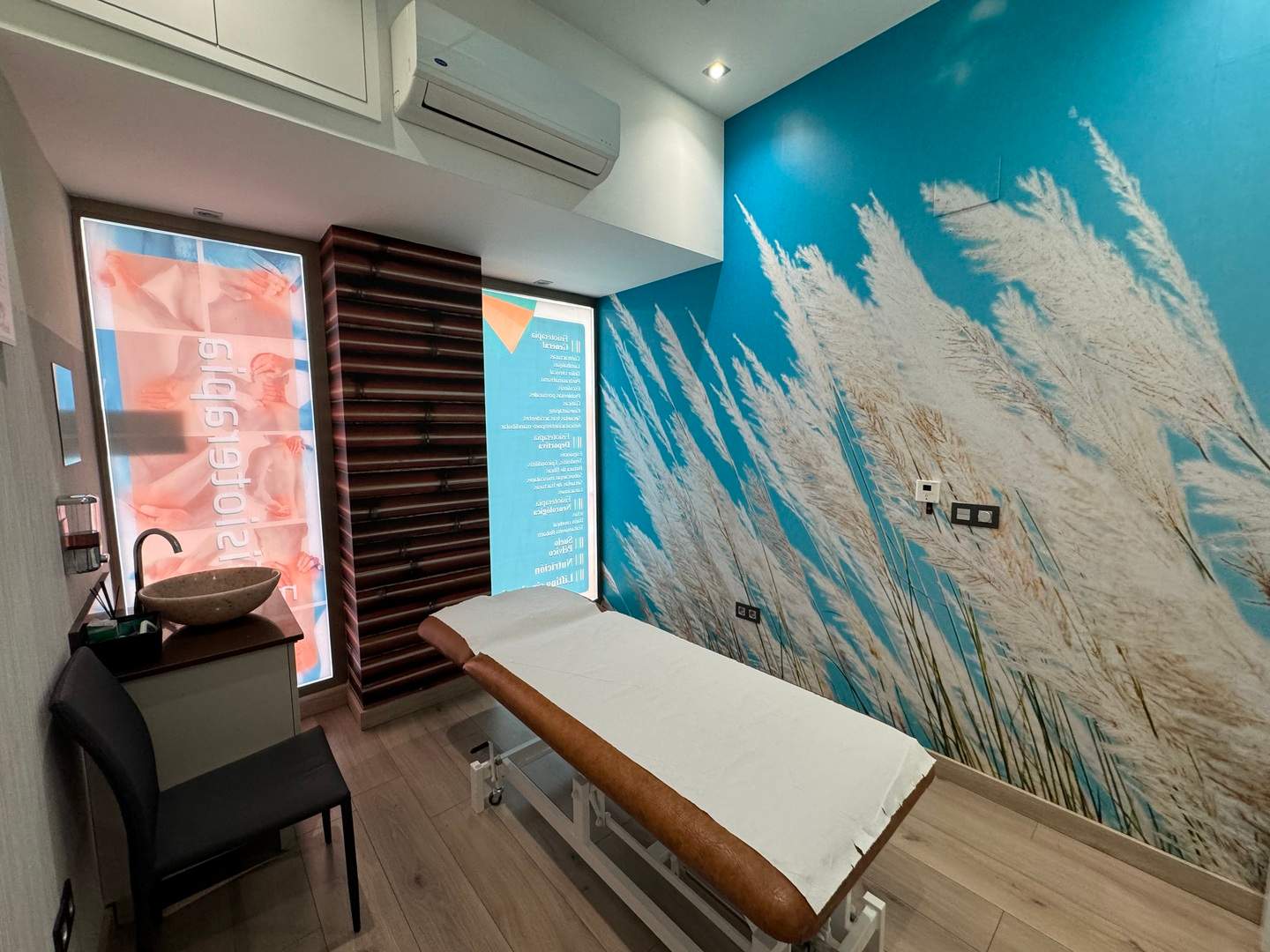 Sala de tratamiento con mural azul de plumeros y panel de bambú vertical